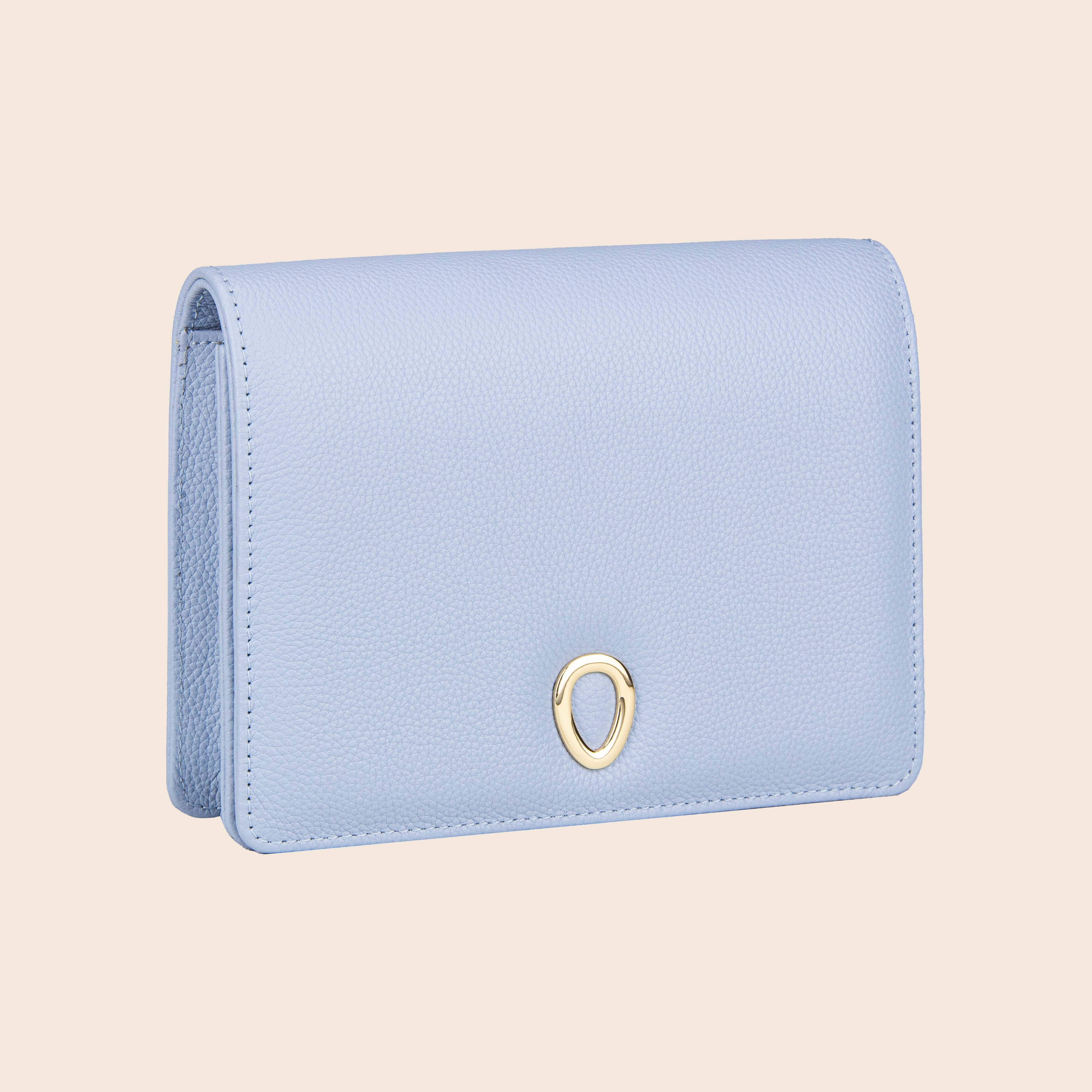 The Vera in leather - Mist Blue is a women's textured leather clutch with a small oval gold emblem on the front, shown against a plain beige background.