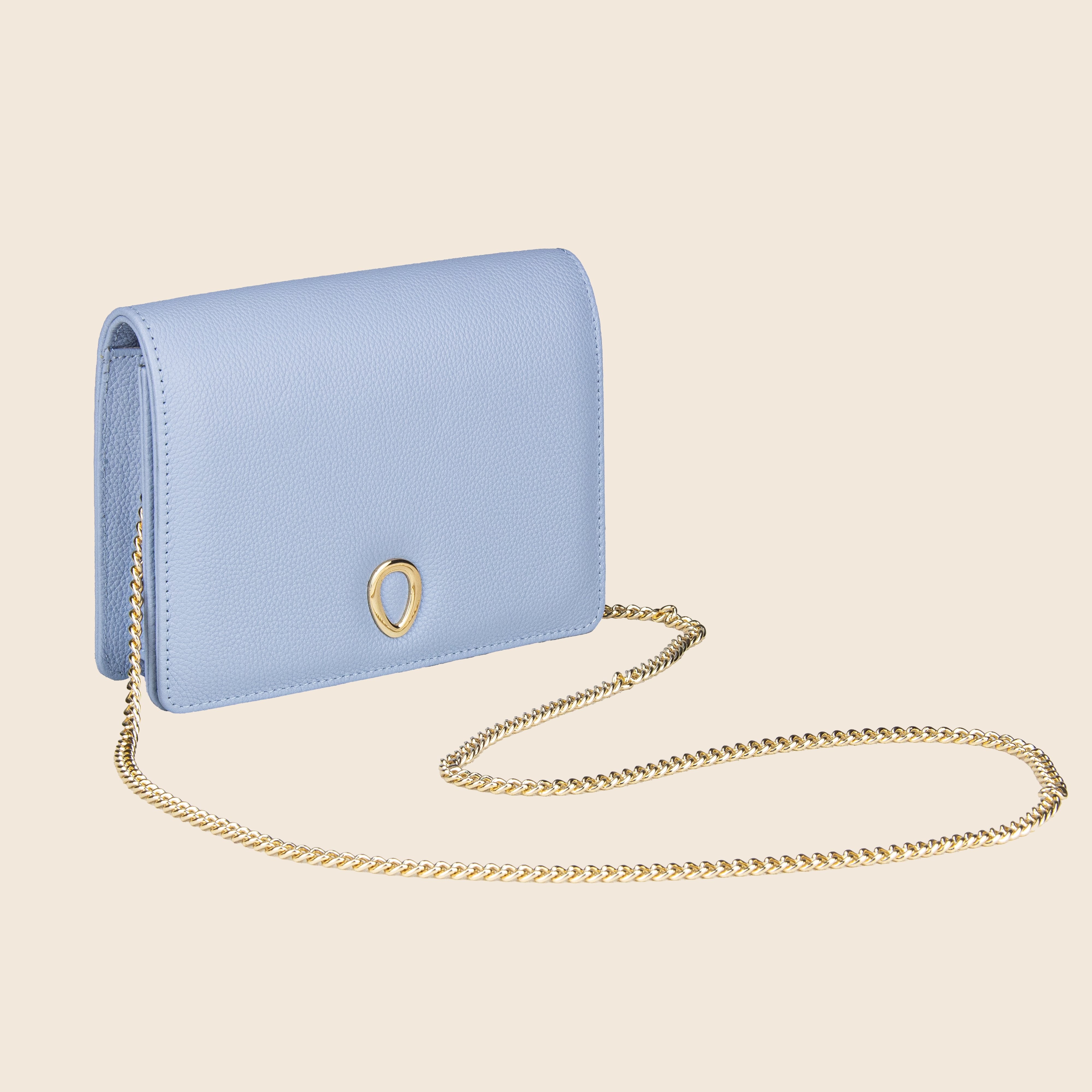 The Vera in leather - Mist Blue is a women's light blue clutch featuring a gold teardrop accent on the front and a long gold chain strap, set against a beige background—an elegant evening bag for any occasion.
