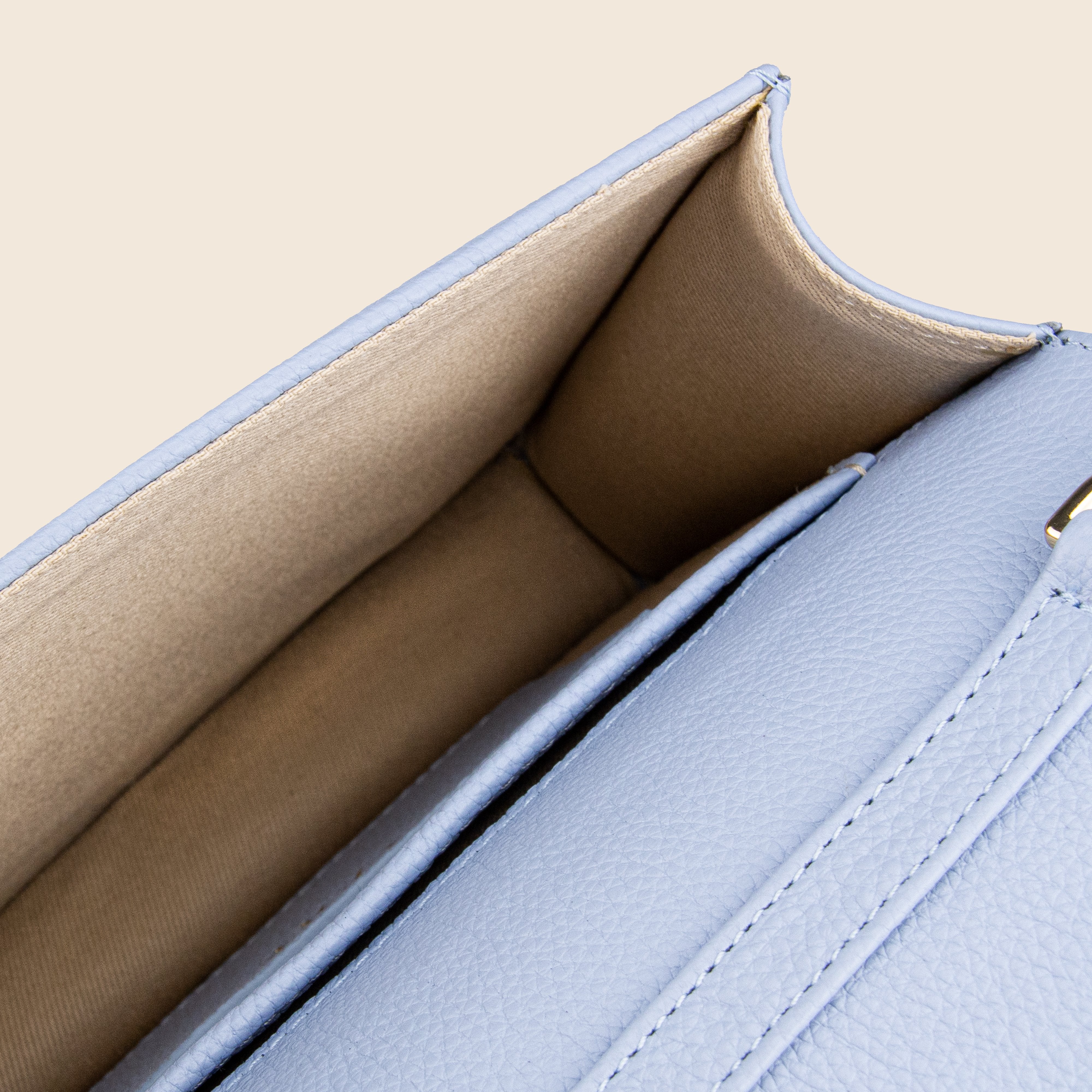 Close-up of the Vera in leather - Mist Blue clutch, featuring an open view of its spacious beige-lined interior and textured light blue leather exterior—an elegant evening bag for any occasion.