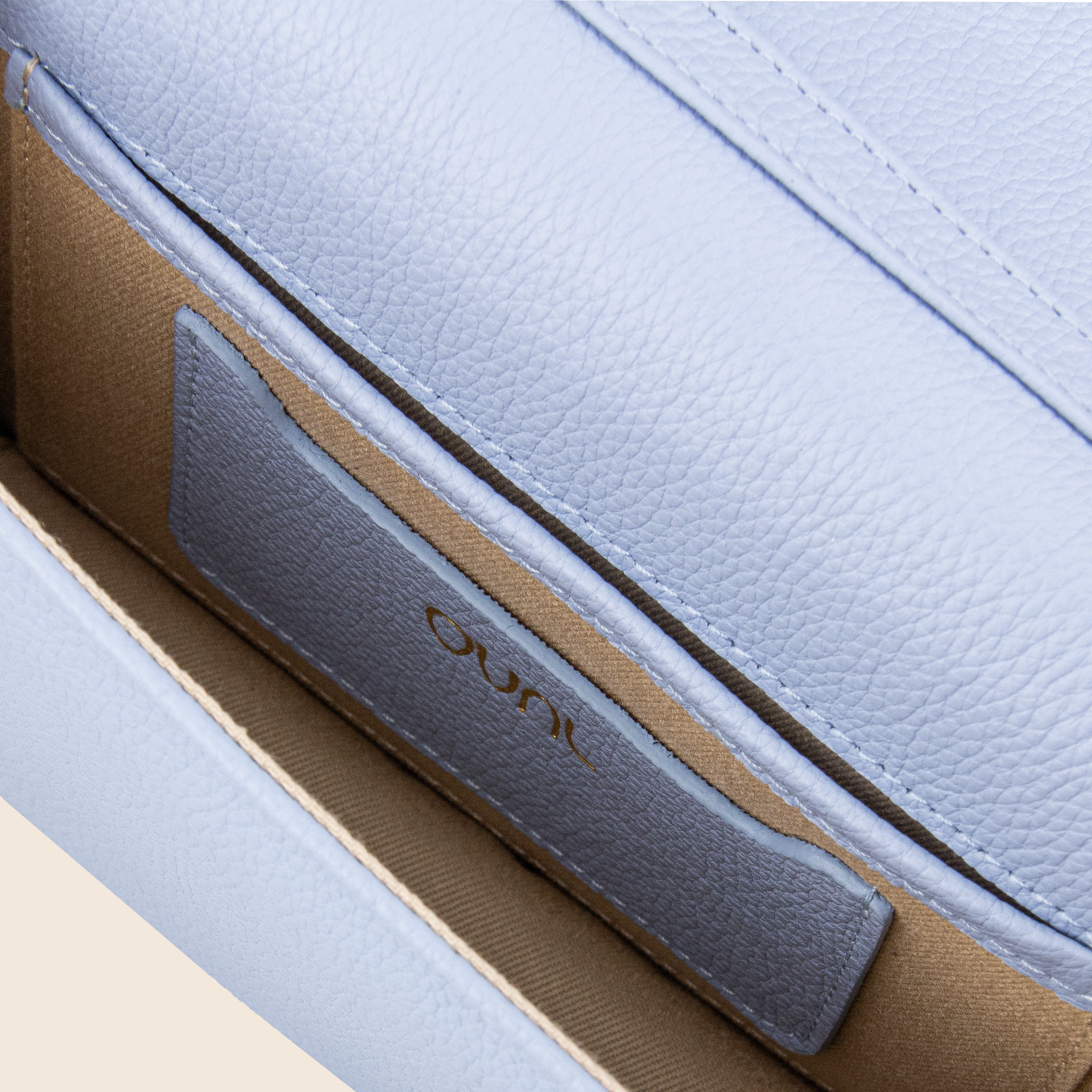 Close-up of Vera in leather - Mist Blue, a women's light blue leather clutch with beige interior, stitched pocket, and a small label reading Ouni.
