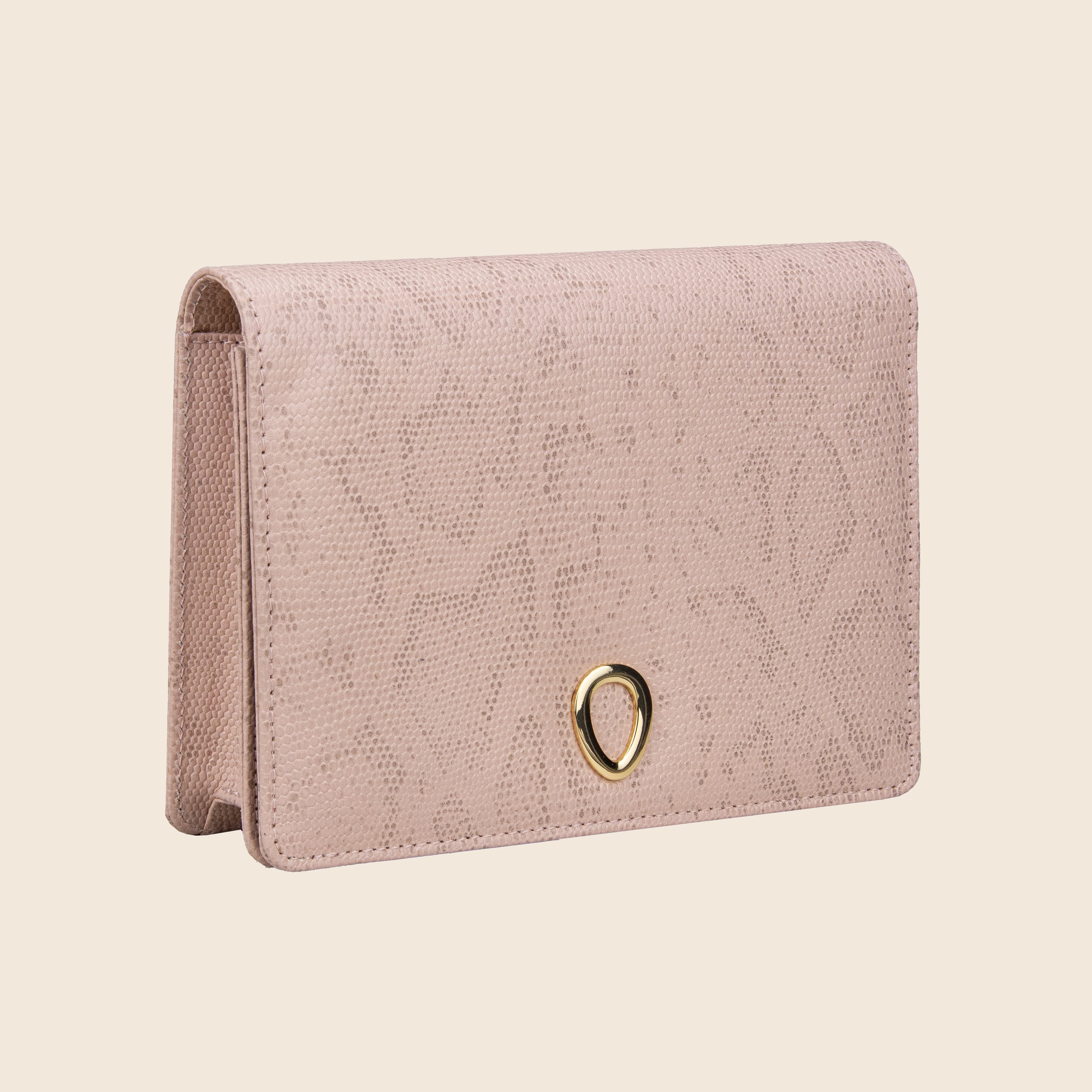 The Vera in leather - Python Rose is a light pink textured women's clutch with a subtle pattern and a gold teardrop-shaped accent on the front, displayed standing on its base against an off-white background.