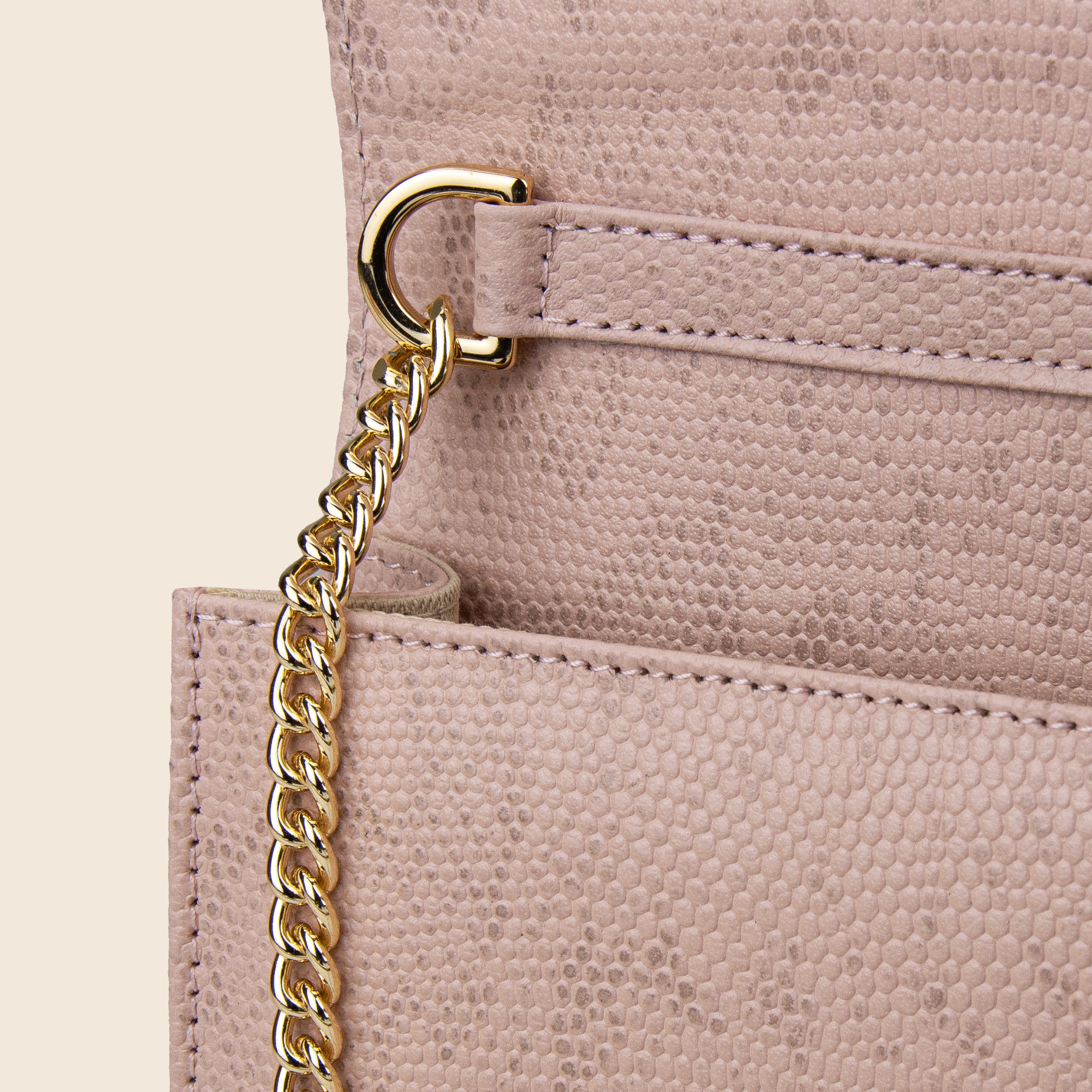 Close-up of the Vera in leather - Python Rose, a beige women's clutch featuring a gold chain strap, gold ring detail, fine stitching, and a faux python pattern on the material.