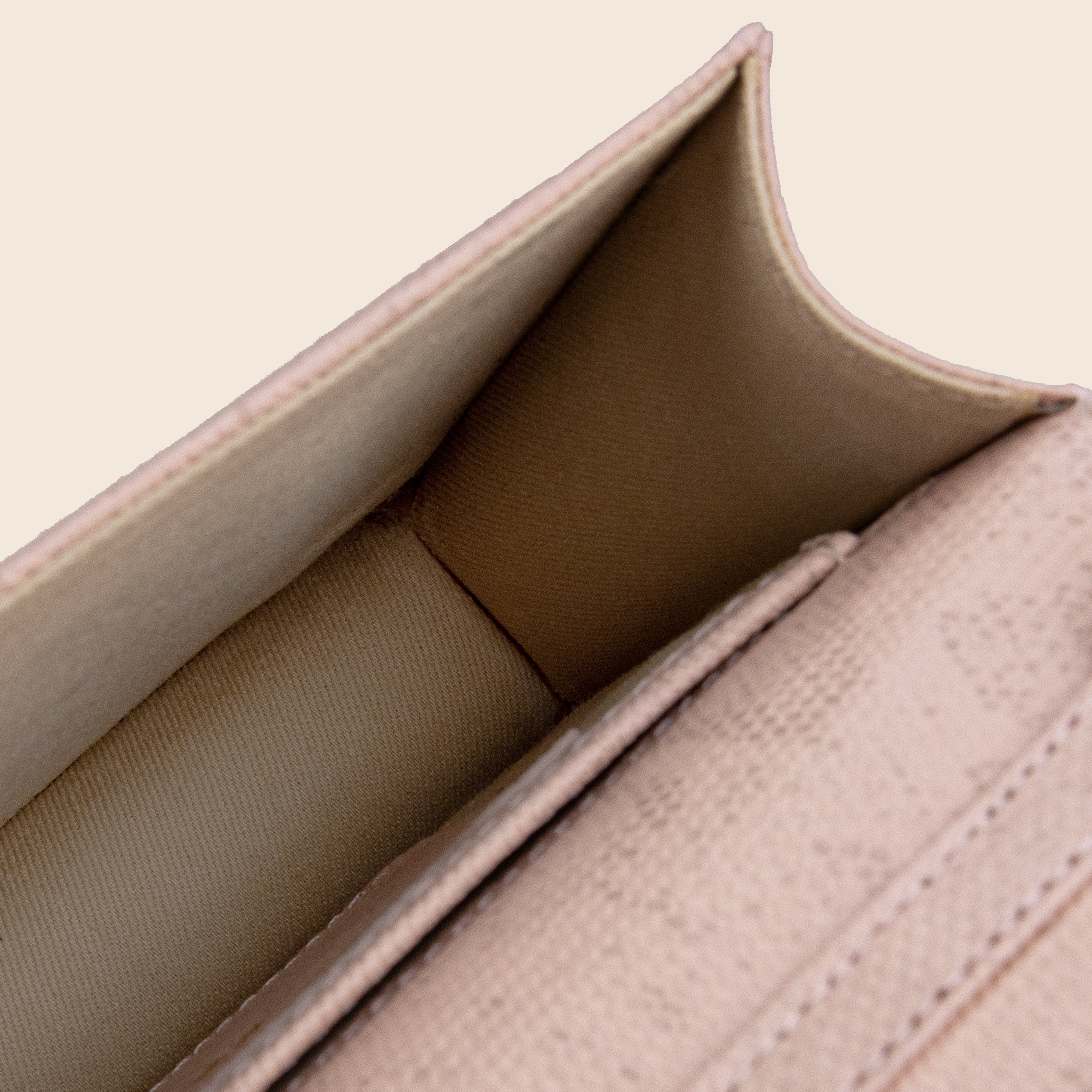 Close-up of the interior of the Vera in leather - Python Rose clutch, featuring an empty beige fabric-lined compartment and detailed stitching.