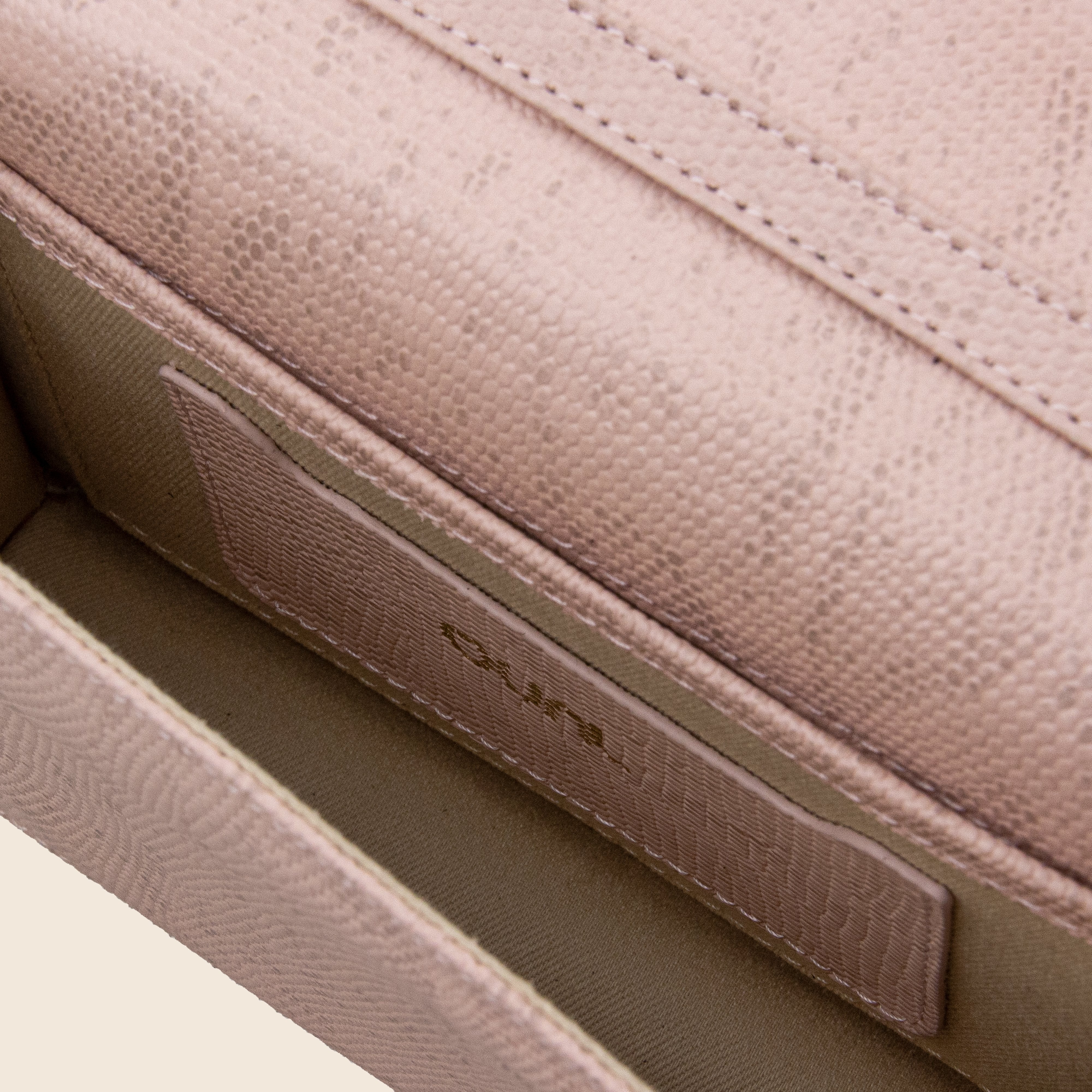 Close-up of the inside of the Vera in leather - Python Rose clutch, featuring textured light pink genuine leather, a fabric lining, an interior pocket, and gold lettering on the pocket.