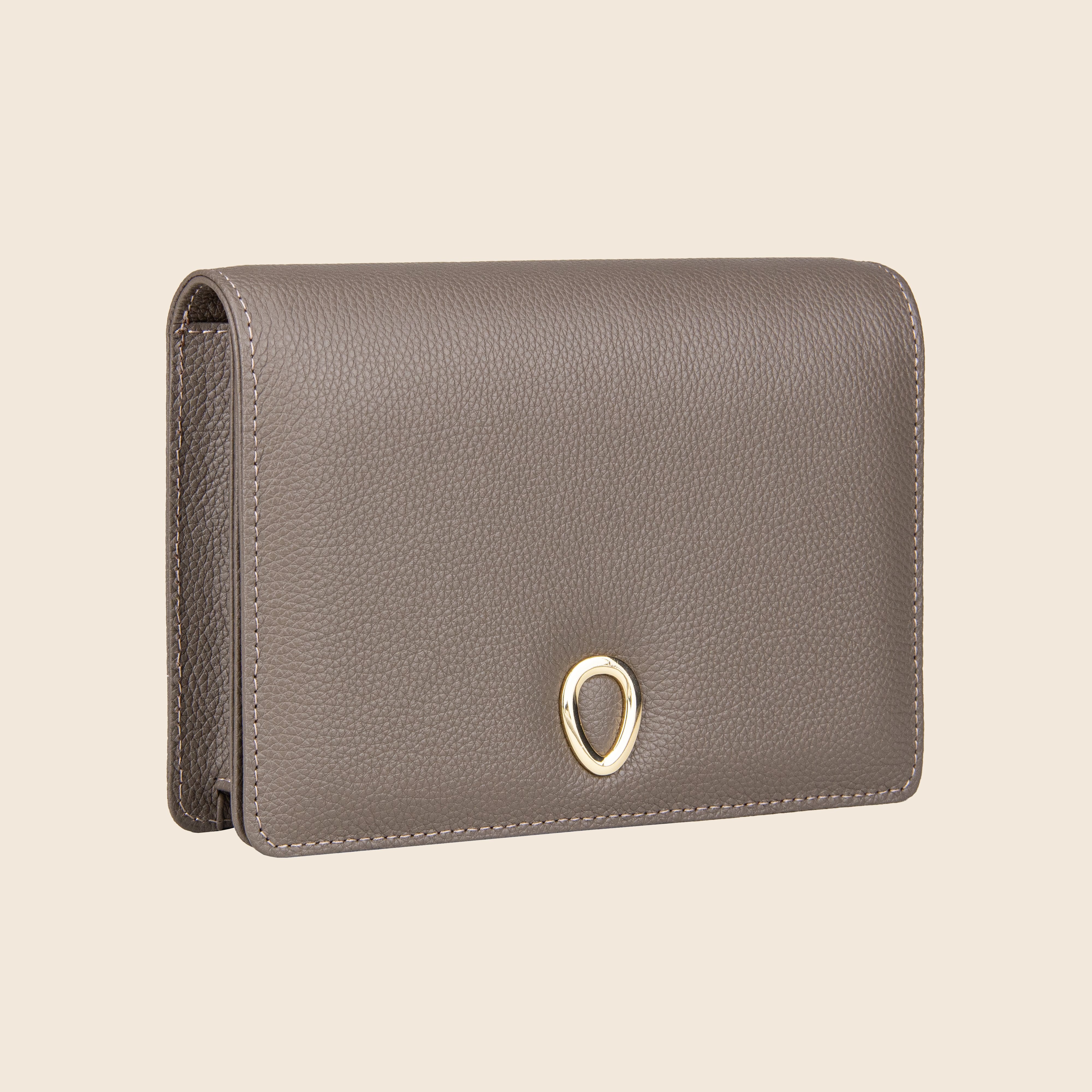 The Vera in leather - Stone Taupe is a taupe genuine leather clutch with a pebbled texture and gold teardrop clasp, shown against a plain beige background.