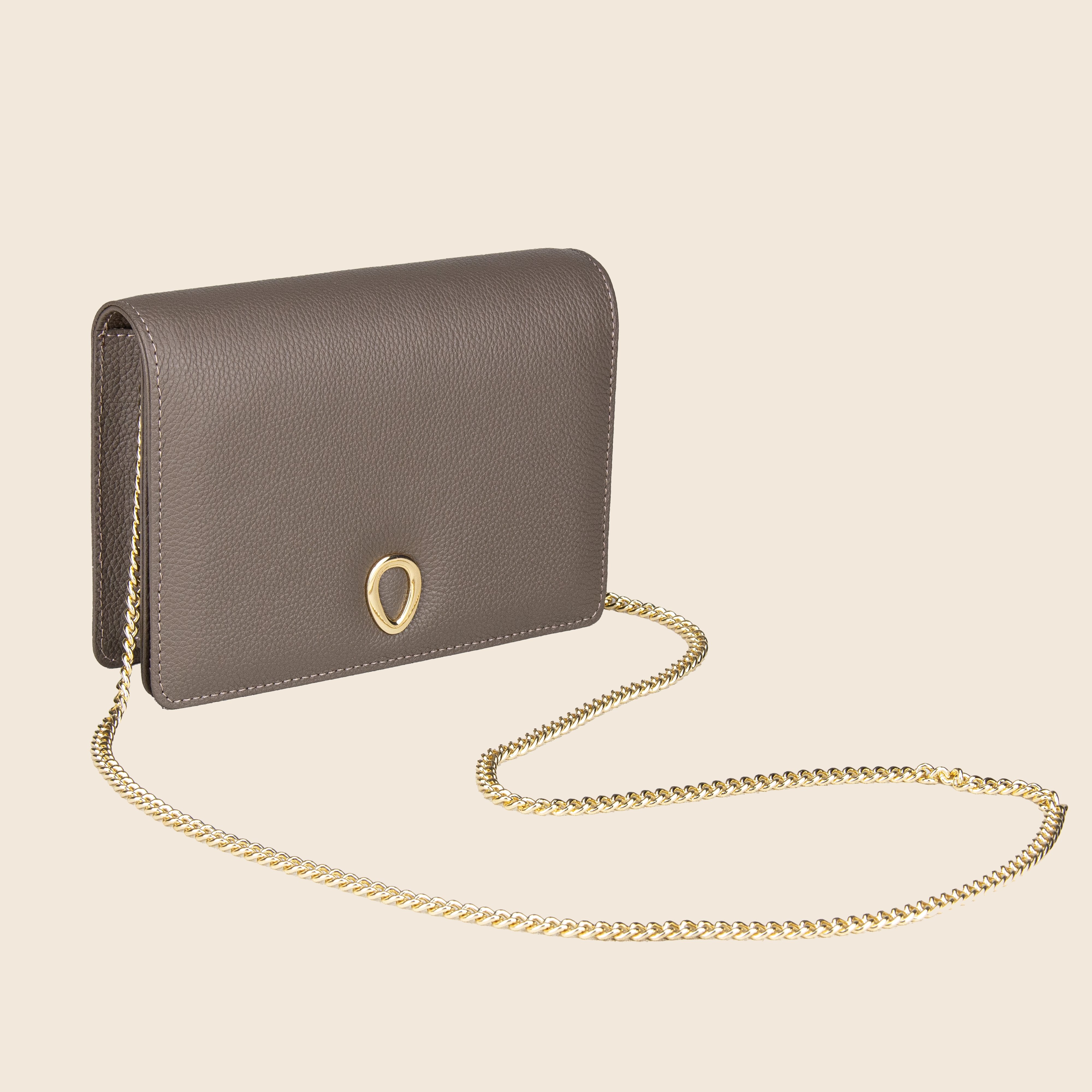 The Vera in leather - Stone Taupe is a genuine taupe leather women’s clutch with a gold chain strap and teardrop-shaped clasp, displayed against a plain beige background for an elegant look.